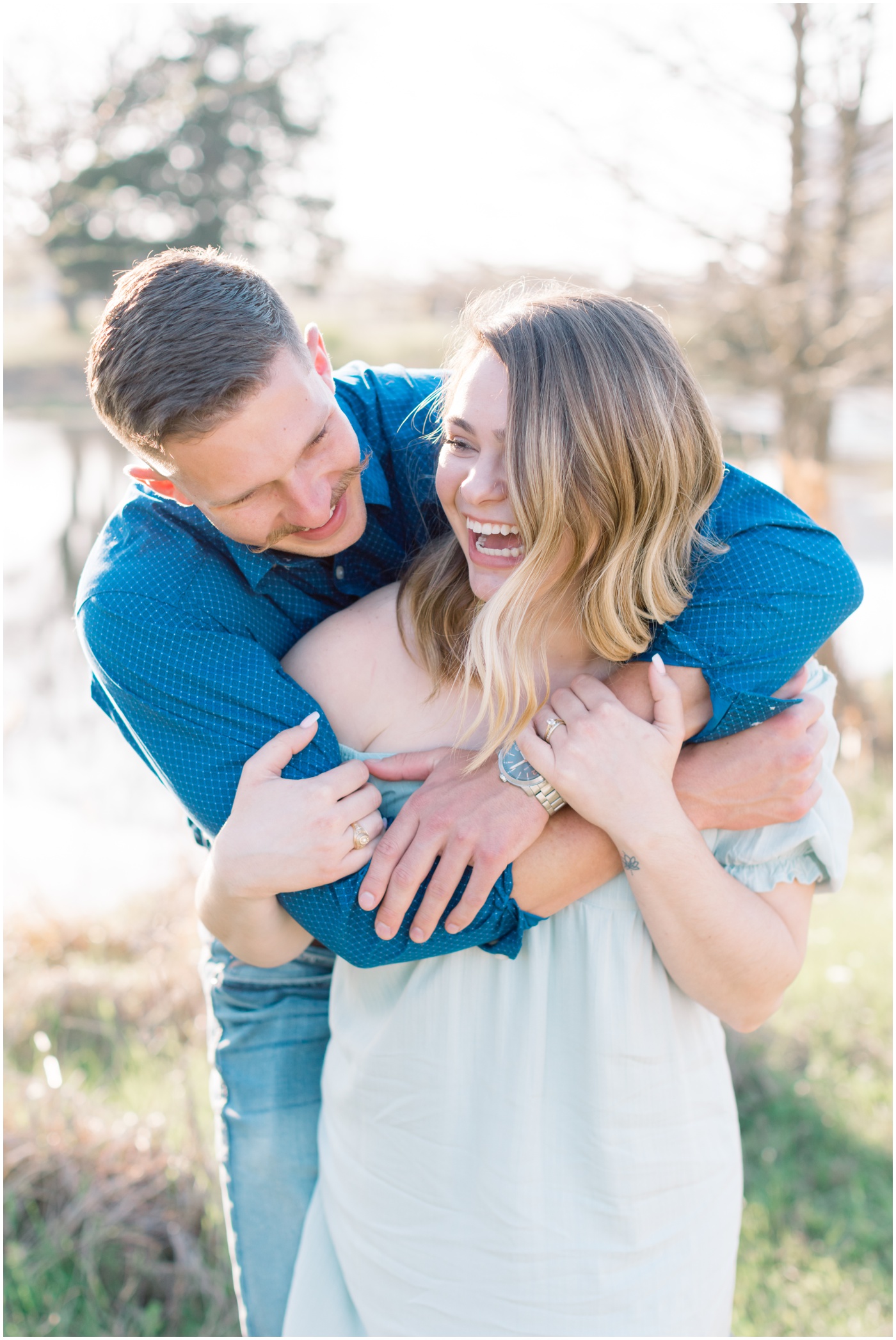 a boy hugs his girlfriend from behind as they laugh together during their college station engagement session