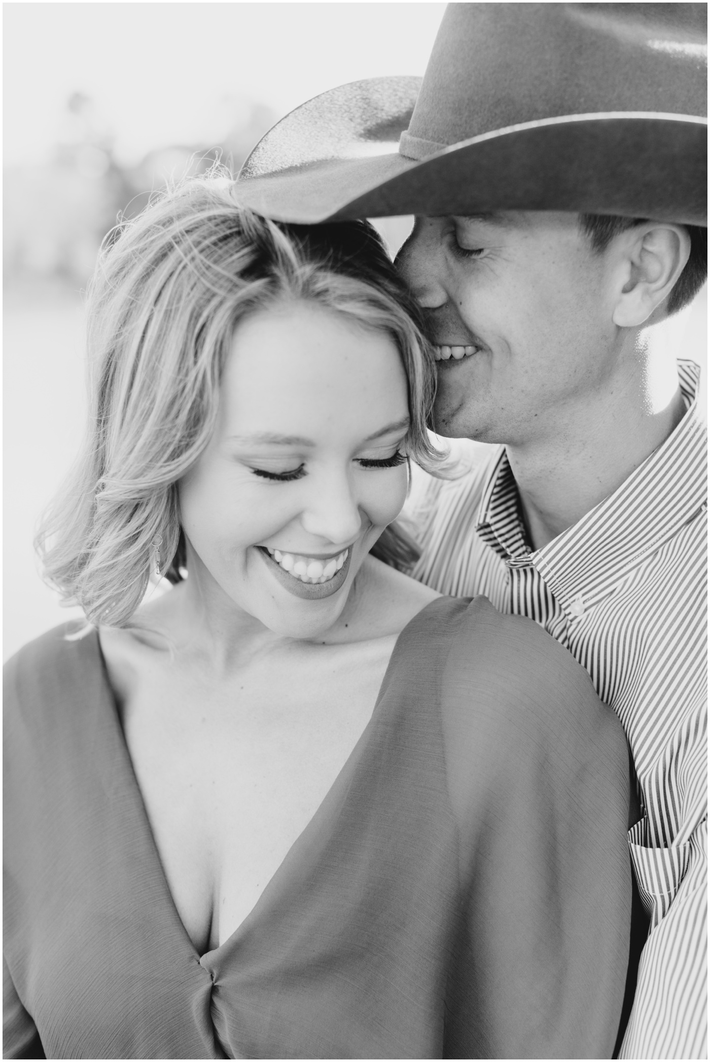 a couple smiles together as the man kisses the side of her head during their engagement session in houston
