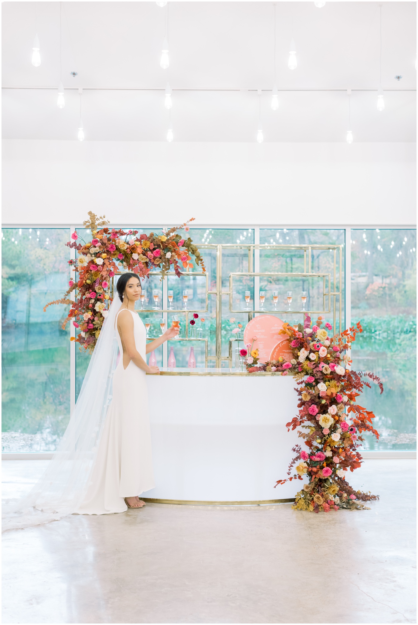 a bride drinking champagne by a floral bar installation