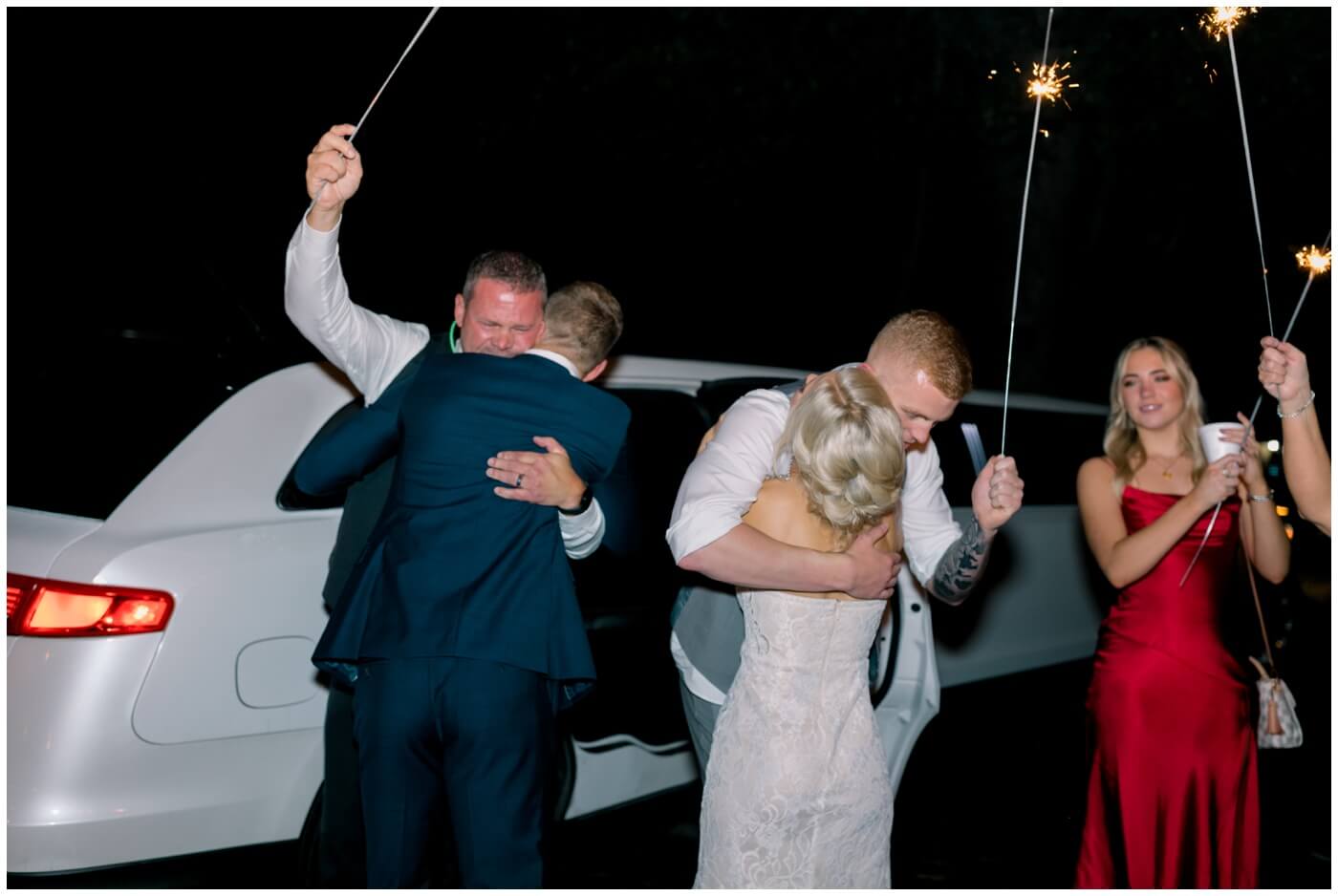 the bride and groom cry as they hug their family at the end of the night 