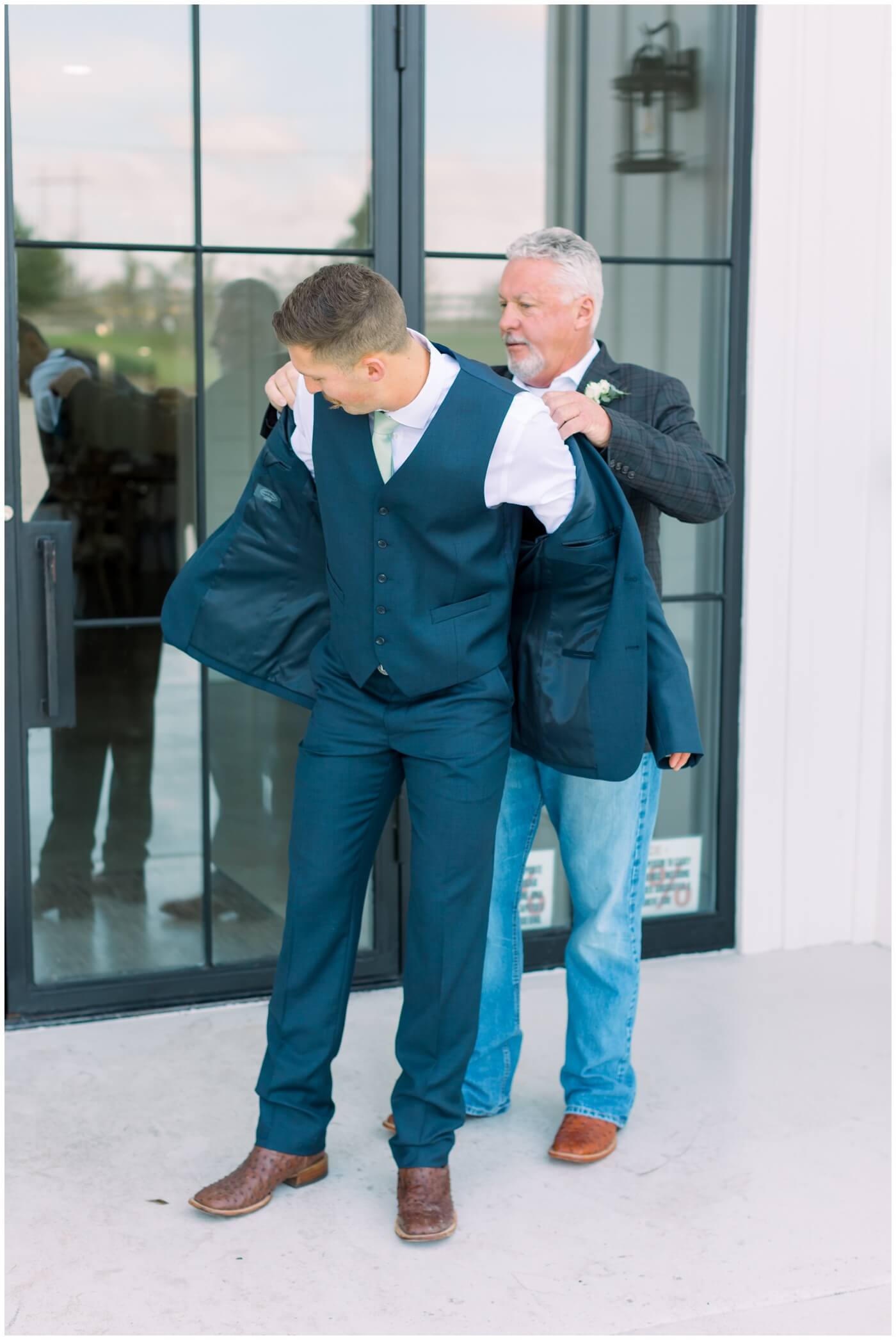 the grooms dad helps his son put his jacket on