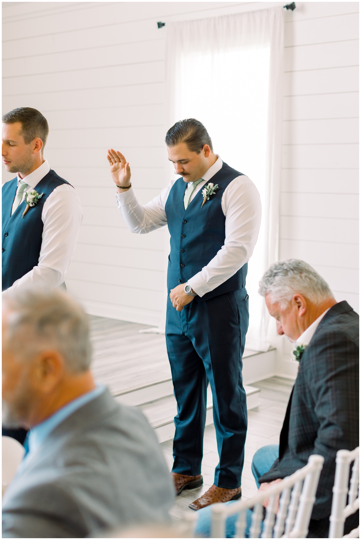 a groomsmen lifts his hand in prayer during the wedding ceremony