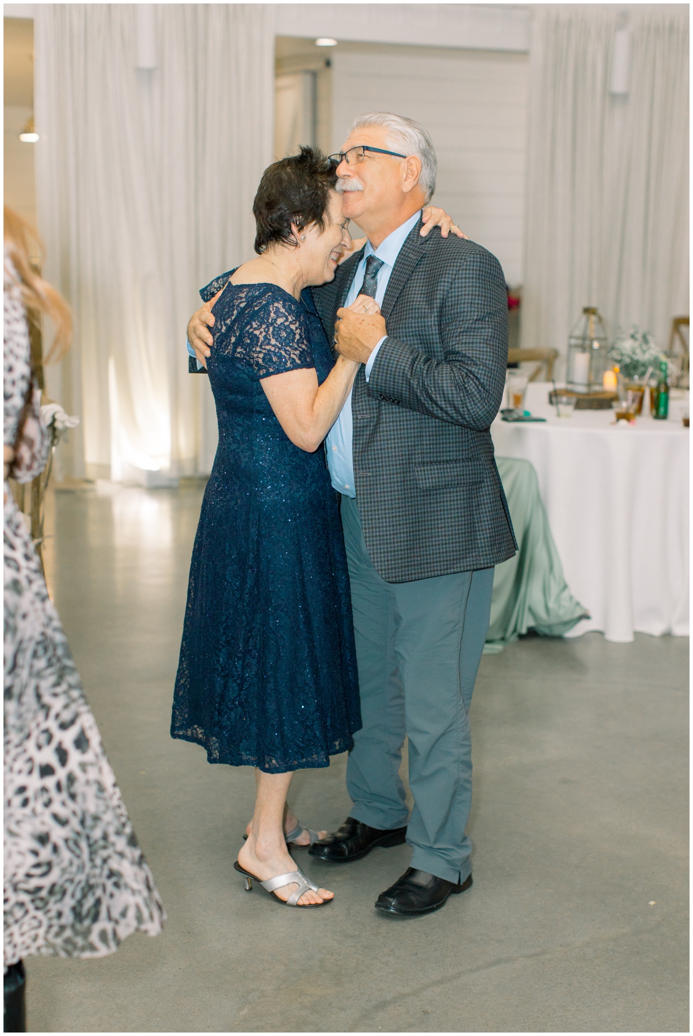 the grandparents of the groom smile as they dance together