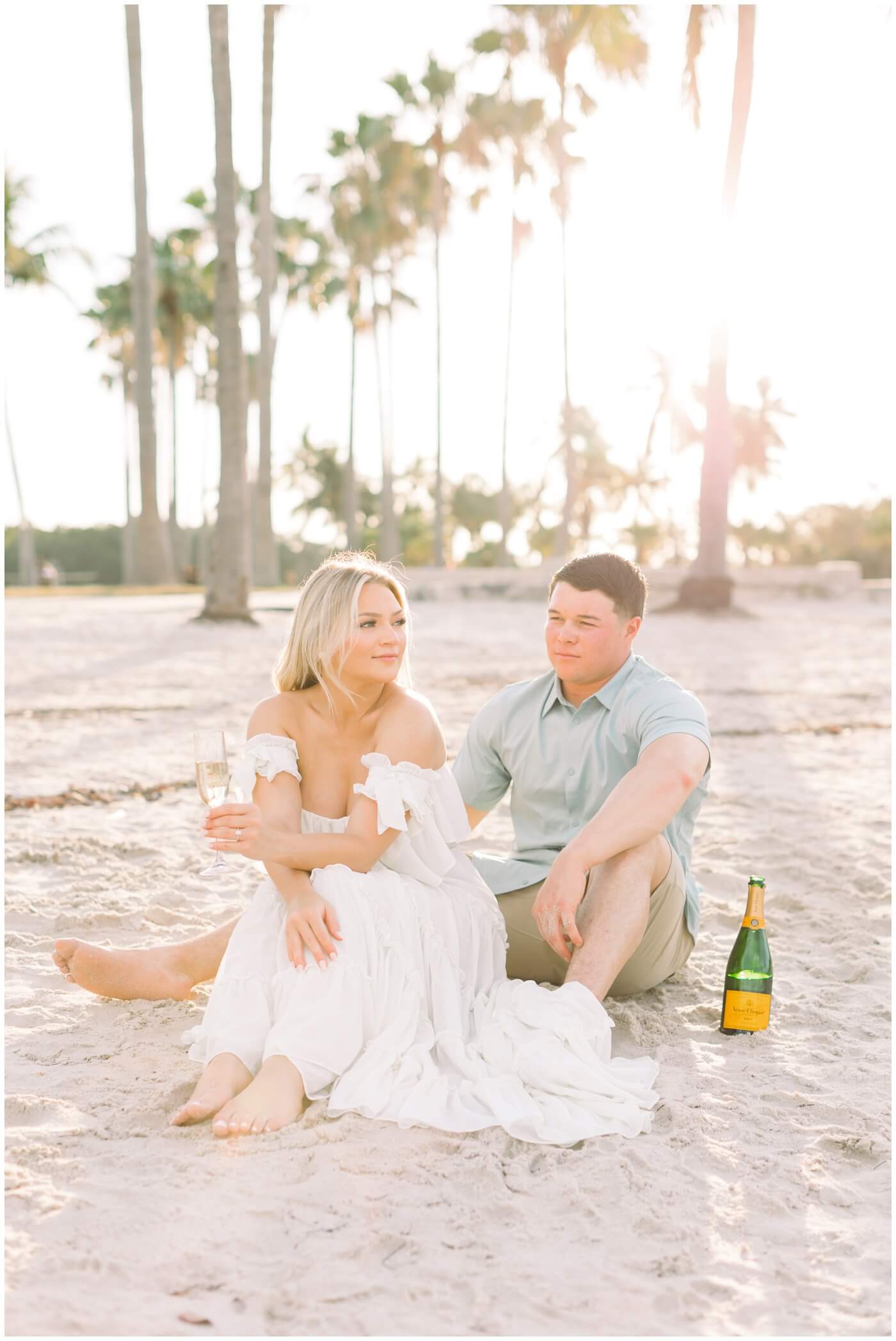 Couple celebrates their engagement with champagne on the beach in Miami.