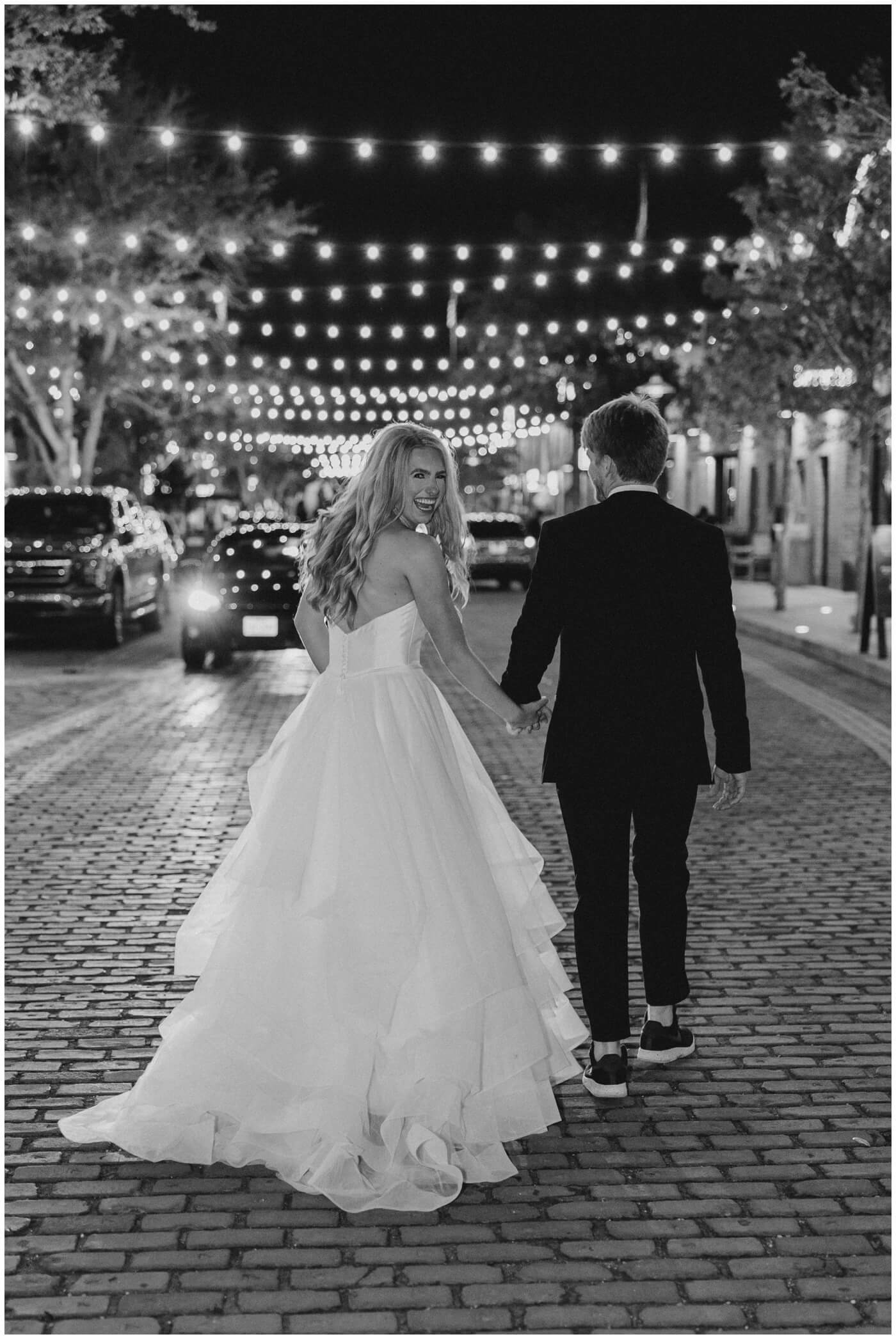 a bride and groom run down the street under lights at night
