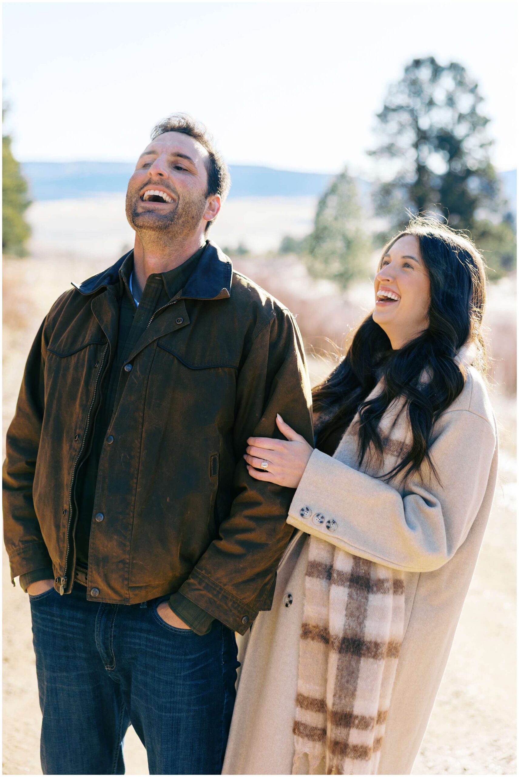 A couple laughs together during their  mountain engagement session in the mountains of New Mexico.